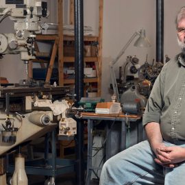 Jonathan Larrabee, the face of HMH Fly Tying Vises, sits with a newly finished vise in his shop at the Pepperell Mill Campus, photographed by Portland Headshot.